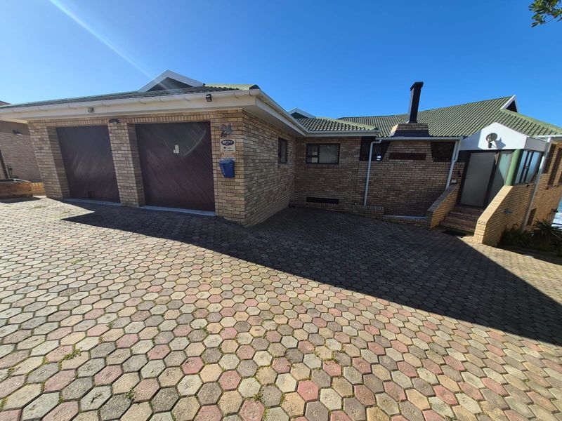 Front exterior view of a brick house featuring a double garage, paved driveway, and an external chimney.
