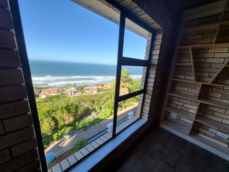 A bright room featuring exposed brick walls, built-in shelving, and a large window offering expansive ocean and coastal views.