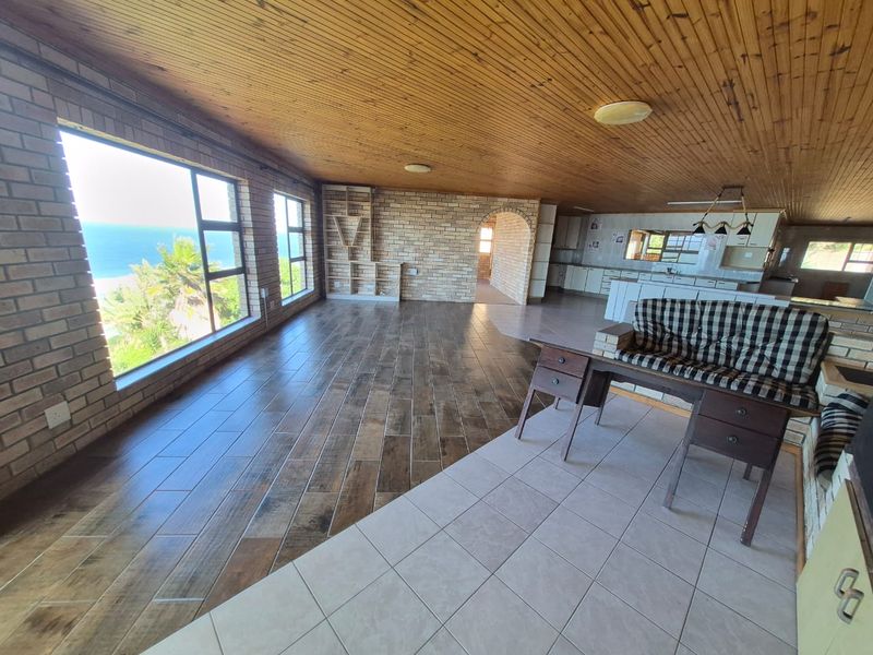 Spacious open-plan living and kitchen area featuring exposed brick walls, timber ceilings, and large windows with ocean views.