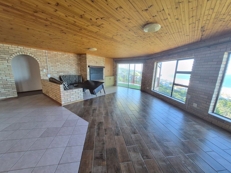 Spacious living area featuring a brick fireplace, timber-clad ceiling, and large windows offering scenic coastal views with direct access to a balcony.