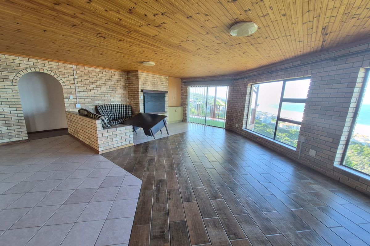 Spacious living area featuring a brick fireplace, timber-clad ceiling, and large windows offering scenic coastal views with direct access to a balcony.