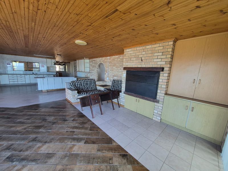 Spacious open-plan living and kitchen area featuring a timber ceiling, brick fireplace, and extensive built-in cabinetry with a mix of tiled flooring.