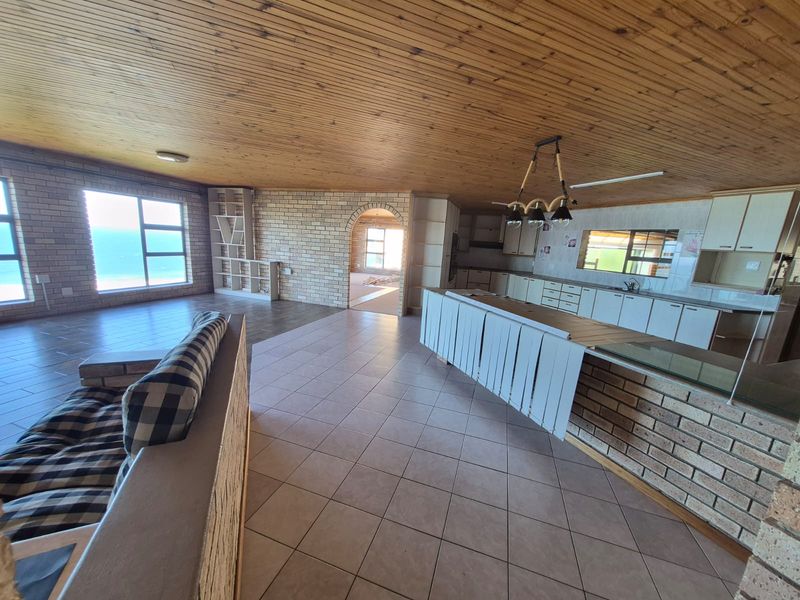 Spacious open-plan living and kitchen area featuring timber-clad ceilings, exposed brick walls, and tiled flooring with ocean views.