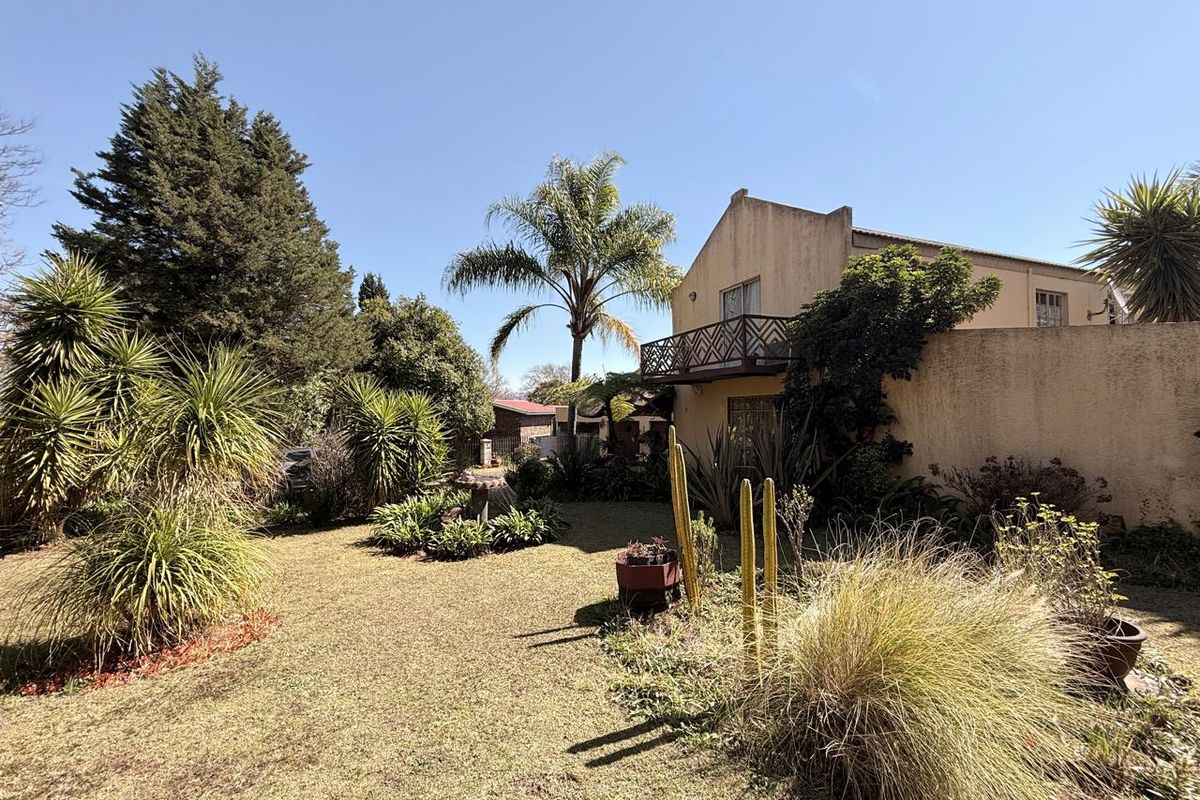 A view of the rear garden featuring a landscaped lawn, mature trees, and a balcony attached to the main building structure.