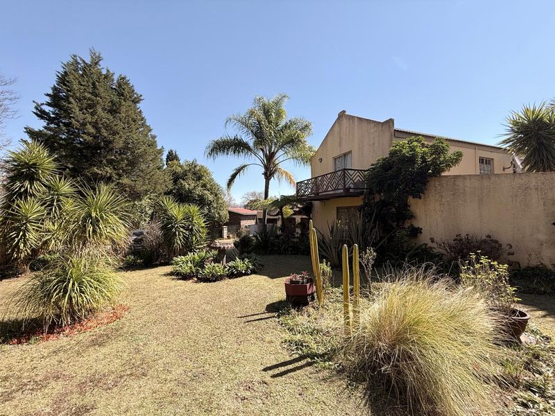 A view of the rear garden featuring a landscaped lawn, mature trees, and a balcony attached to the main building structure.