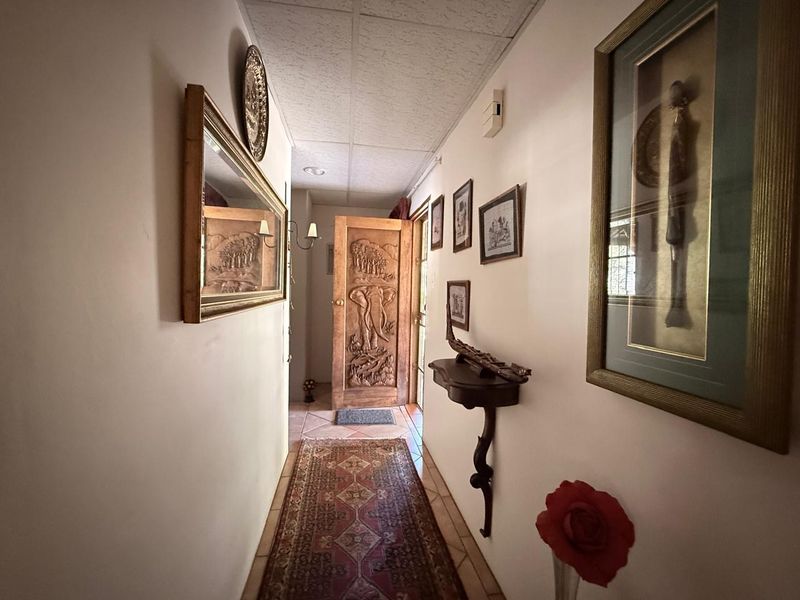 A narrow hallway featuring tiled flooring, acoustic ceiling tiles, and a decorative carved wooden door leading to the exterior.