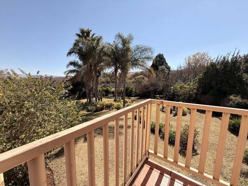 An elevated balcony with a simple railing overlooking a spacious garden with mature palm trees and established landscaping.