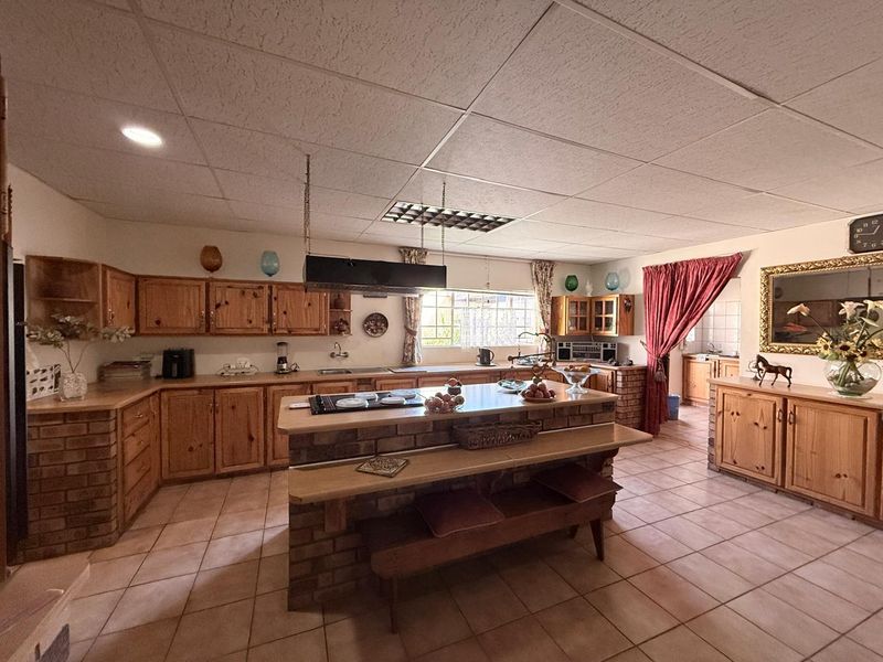 Spacious kitchen featuring rustic pine cabinetry, a central brick island with a built-in hob, and tiled flooring throughout.