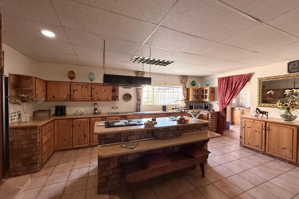Spacious kitchen featuring rustic pine cabinetry, a central brick island with a built-in hob, and tiled flooring throughout.