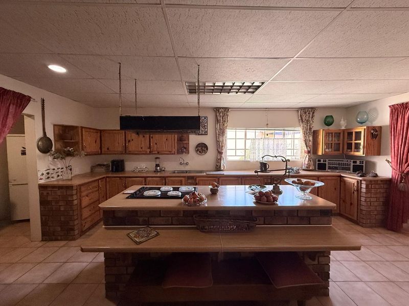 Spacious kitchen featuring extensive wooden cabinetry, a central brick island with a built-in hob, and tiled flooring throughout.