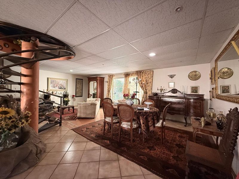 Spacious open-plan living and dining area featuring a distinctive spiral staircase, tiled flooring, and a drop ceiling with recessed lighting.