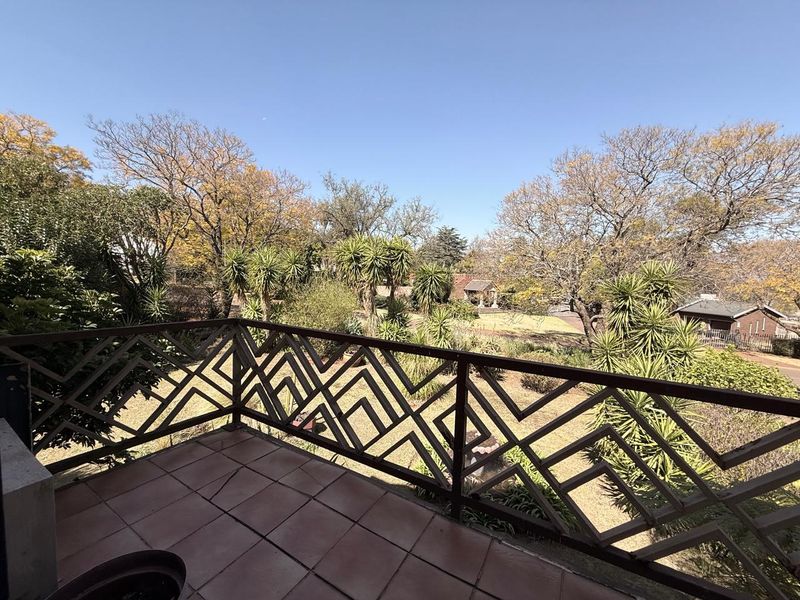 An elevated balcony featuring tiled flooring and a decorative metal balustrade, offering pleasant views over the surrounding garden and mature trees.