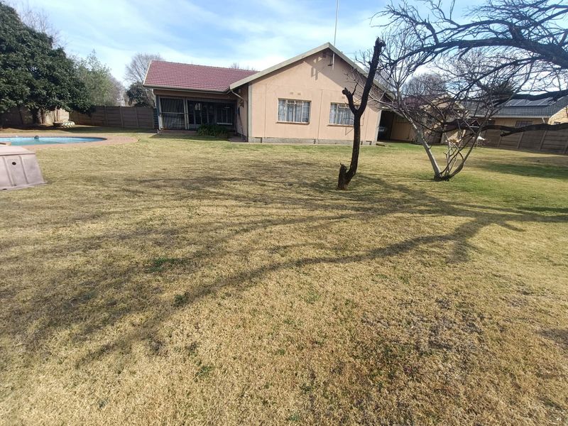 Rear view of the property featuring a spacious garden, swimming pool with paved surround, and a tiled roof structure.