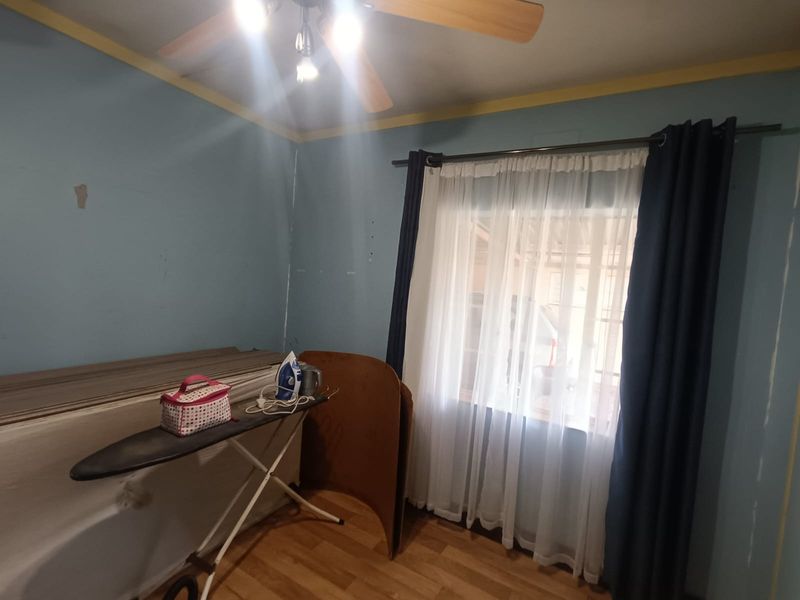 A bedroom featuring laminate flooring and a ceiling fan, currently requiring cosmetic updates to the wall finishes.