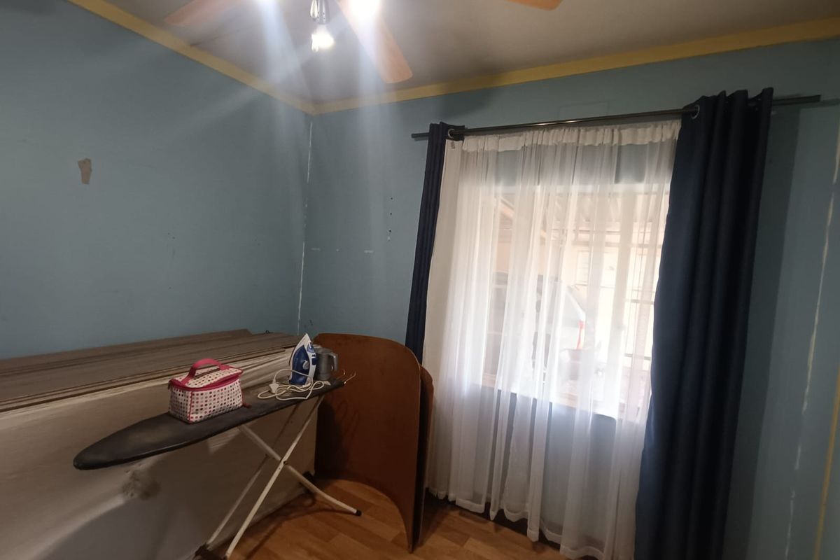 A bedroom featuring laminate flooring and a ceiling fan, currently requiring cosmetic updates to the wall finishes.