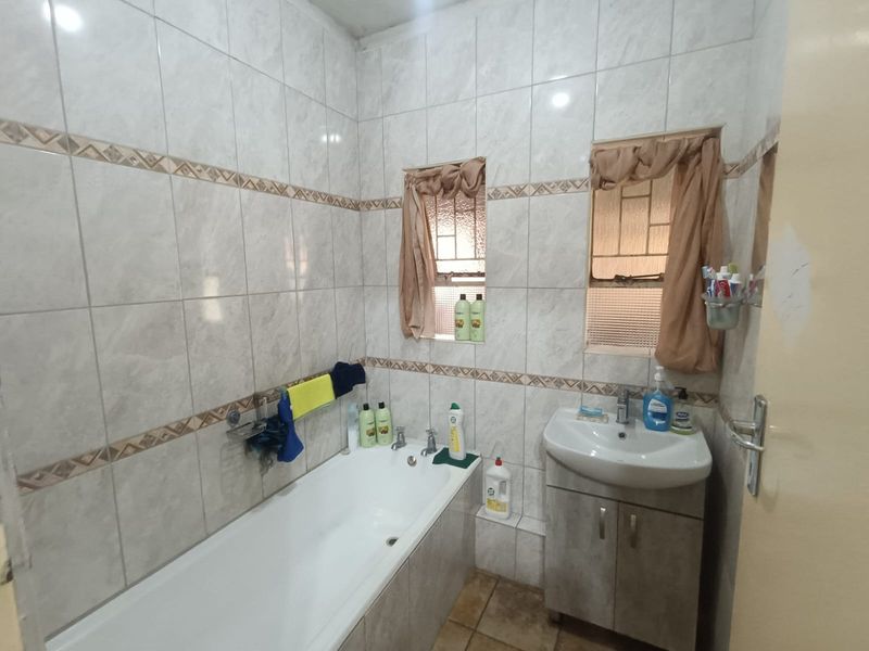 A functional bathroom featuring a built-in bathtub, a vanity cabinet with a basin, and full-height wall tiling.