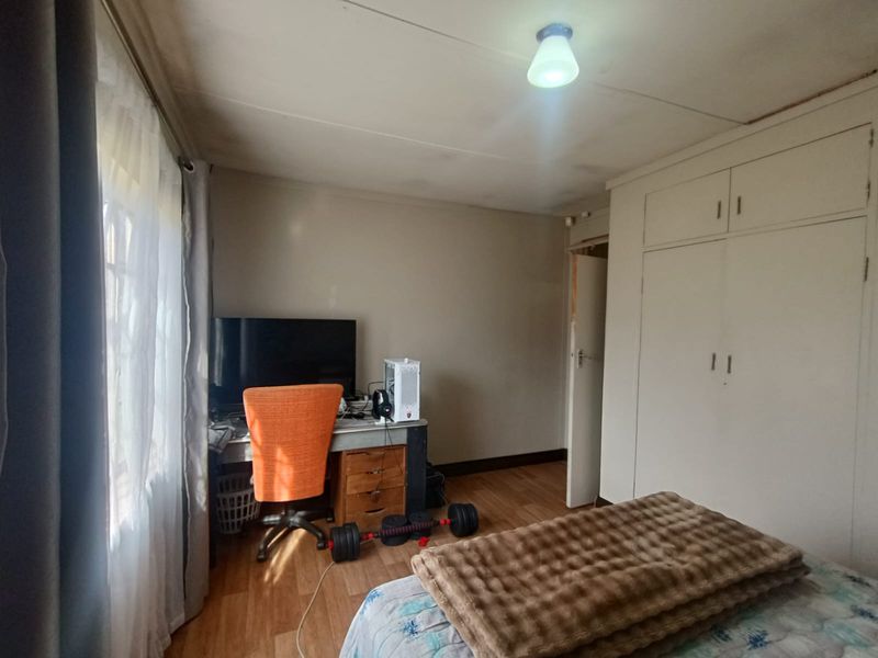 A bedroom featuring laminate flooring, built-in cupboards, and a ceiling light fixture, showing signs of wear and ceiling staining.