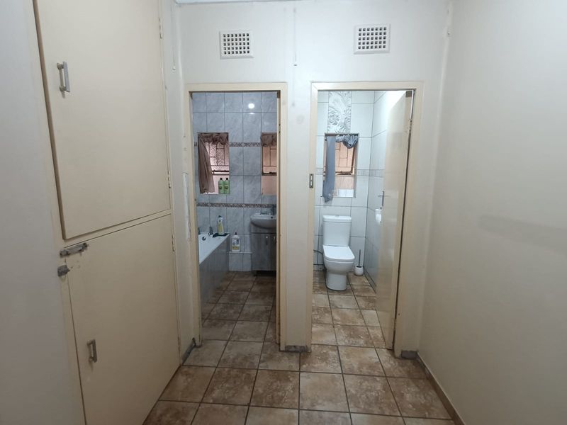 A hallway featuring built-in storage cupboards with direct access to a separate bathroom and toilet area with tiled flooring.