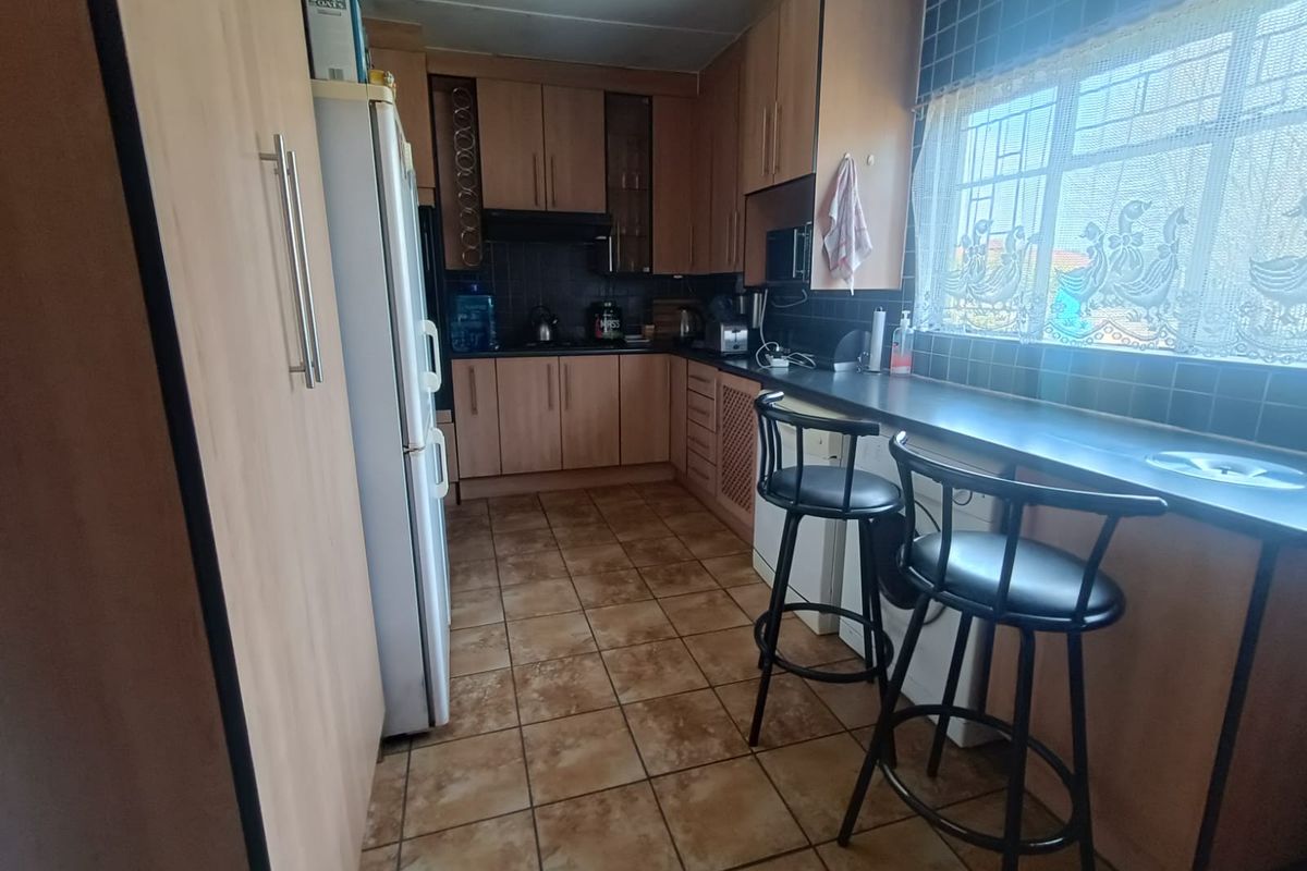 A functional kitchen featuring laminate cabinetry, tiled backsplash, tiled flooring, and a built-in breakfast bar with security bars on the window.