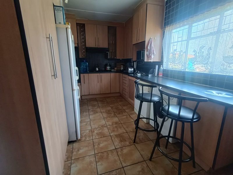 A functional kitchen featuring laminate cabinetry, tiled backsplash, tiled flooring, and a built-in breakfast bar with security bars on the window.