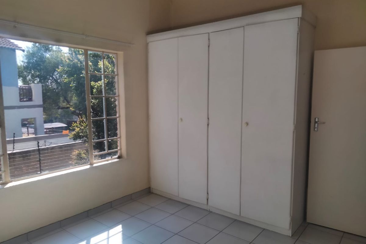 A bright, empty bedroom featuring tiled flooring, a large built-in wardrobe, and a window providing natural light and a view of the exterior.