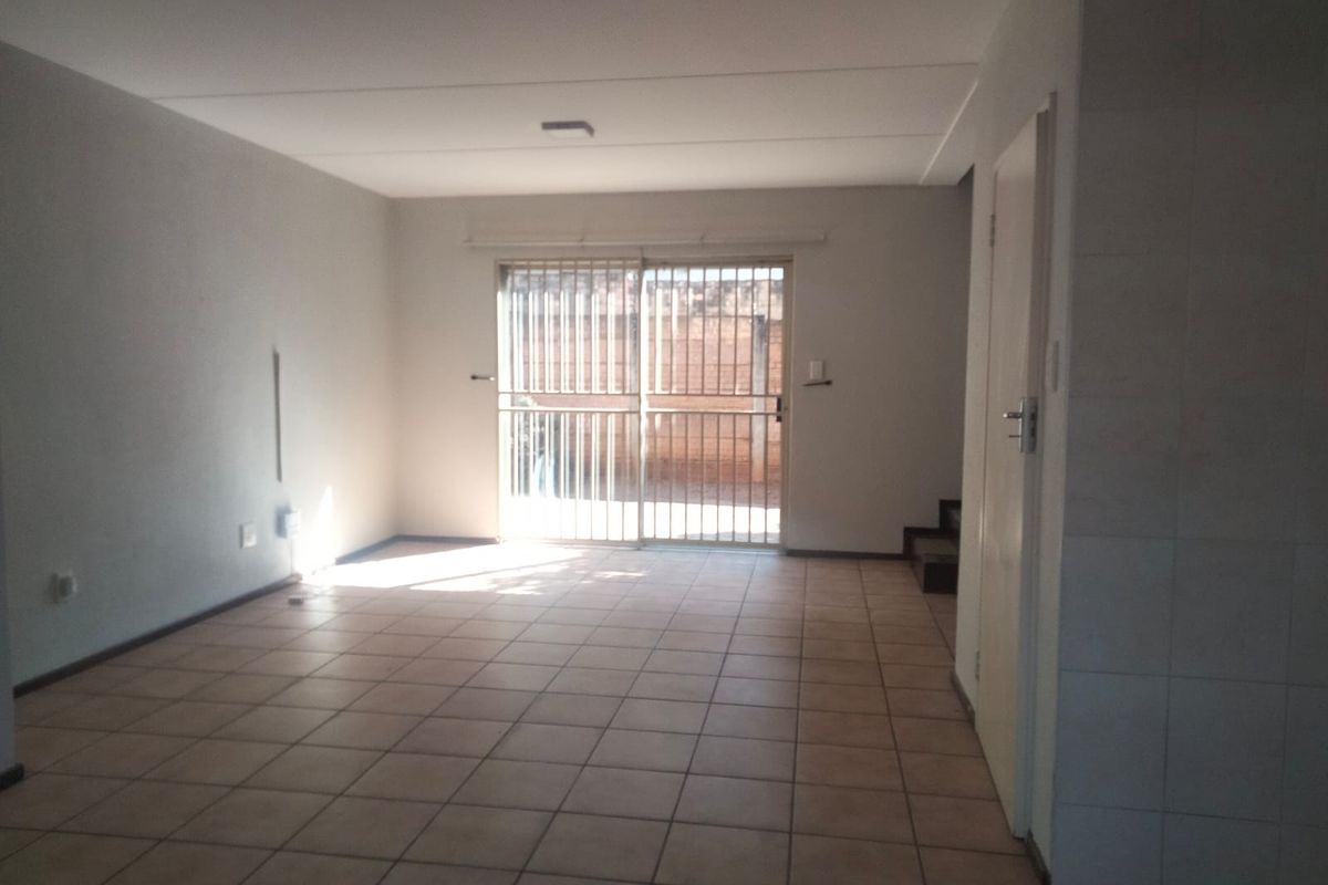 An empty, open-plan living area featuring tiled flooring and a sliding glass door with a security gate leading to the exterior.