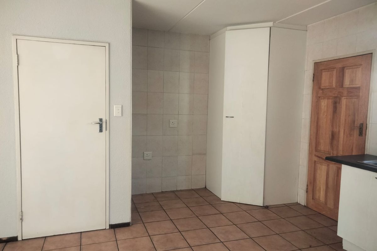 A functional kitchen area featuring tiled flooring, a built-in corner cupboard, and tiled splashbacks, currently presented as an empty, blank canvas.
