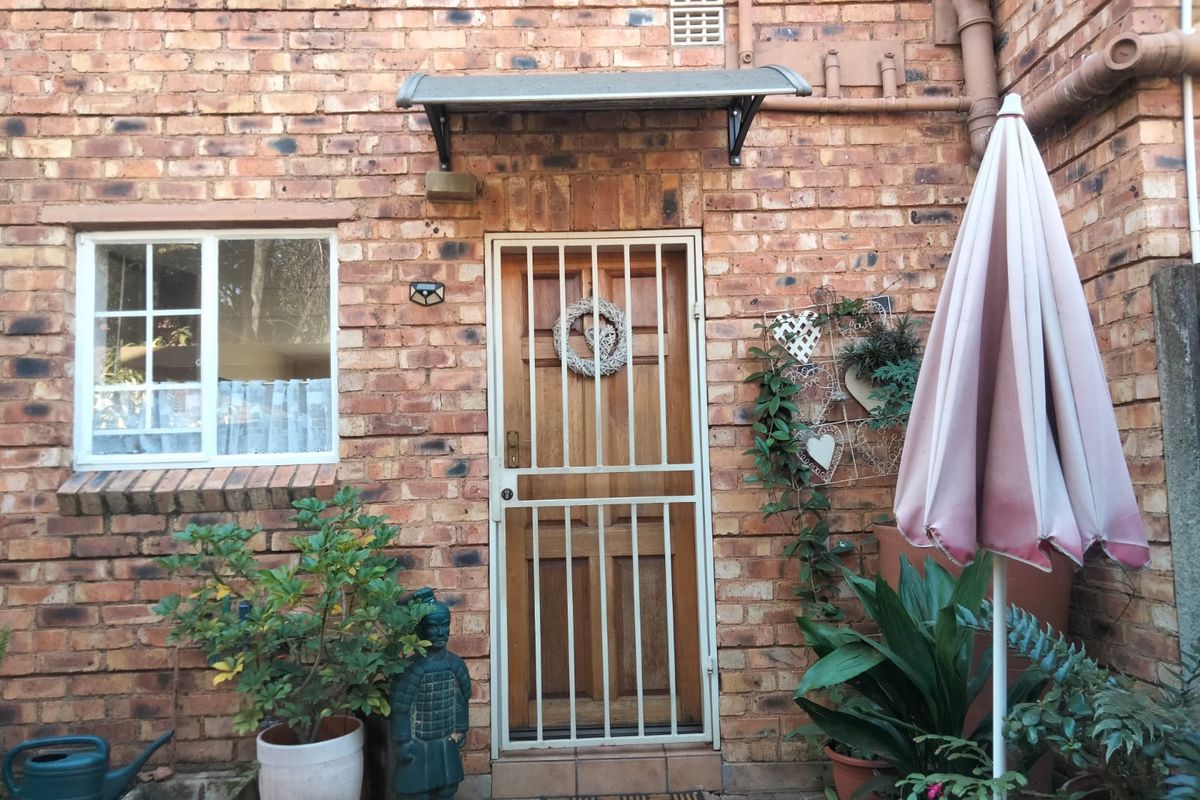 A rear exterior view of a townhouse featuring a face brick facade, a secure timber entrance door with a metal security gate, and a small awning.