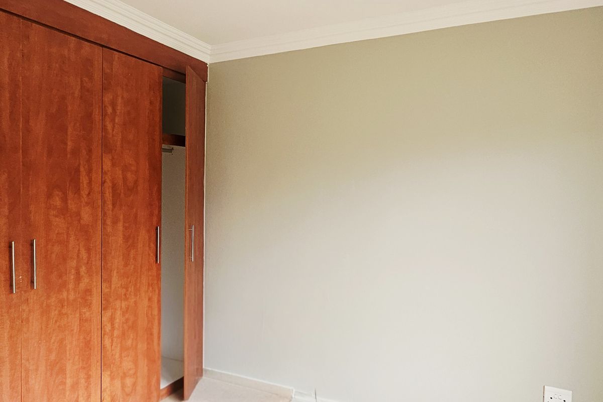A clean, empty bedroom featuring a large built-in wooden wardrobe with modern handles and neutral wall finishes.