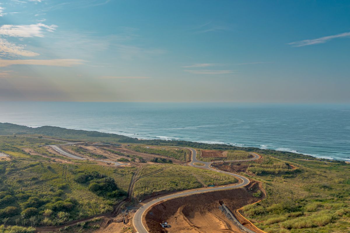 Aerial view of a coastal development site featuring winding paved roads, natural vegetation, and direct ocean views.