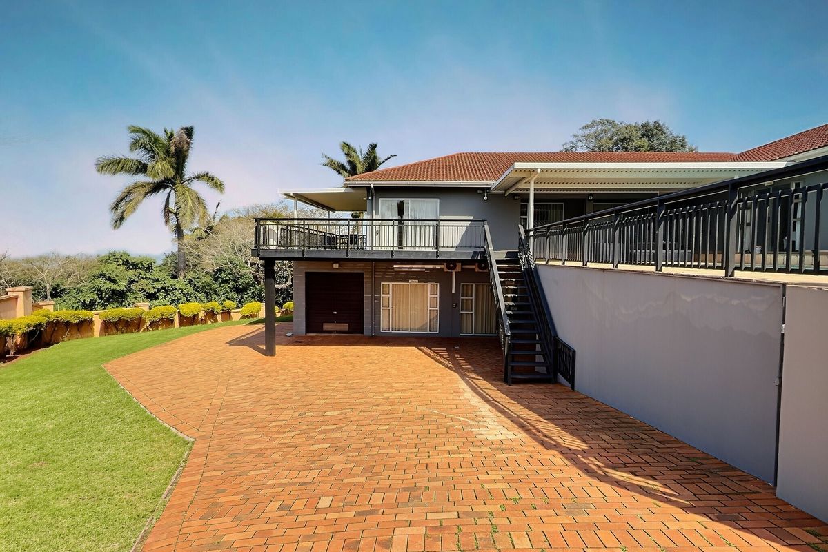 Rear view of the guest house featuring a spacious brick-paved driveway, raised balcony with metal railings, and external staircase access.