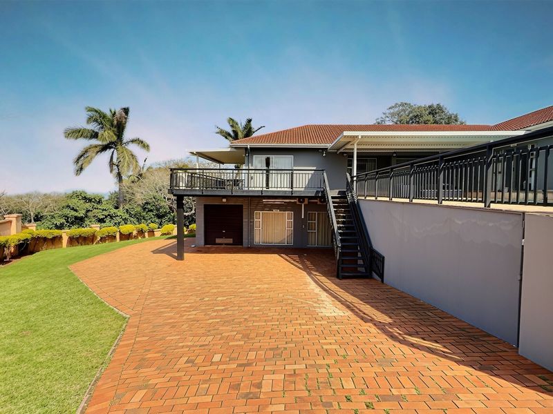 Rear view of the guest house featuring a spacious brick-paved driveway, raised balcony with metal railings, and external staircase access.
