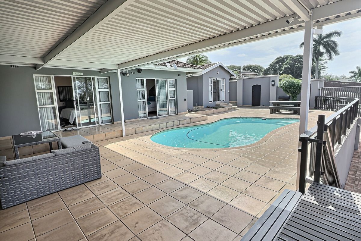 Spacious covered patio area overlooking a swimming pool, featuring tiled flooring and direct access to guest house rooms through sliding glass doors.