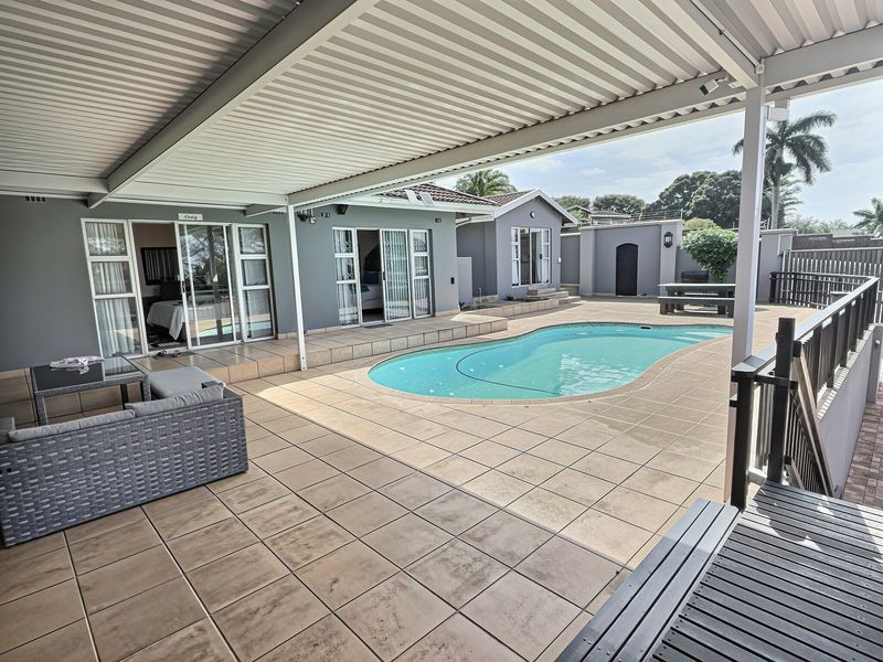 Spacious covered patio area overlooking a swimming pool, featuring tiled flooring and direct access to guest house rooms through sliding glass doors.