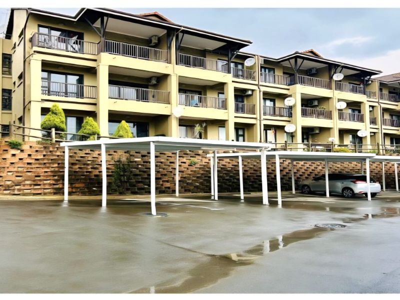 Exterior view of a multi-story townhouse complex featuring covered parking bays and a tiered retaining wall.