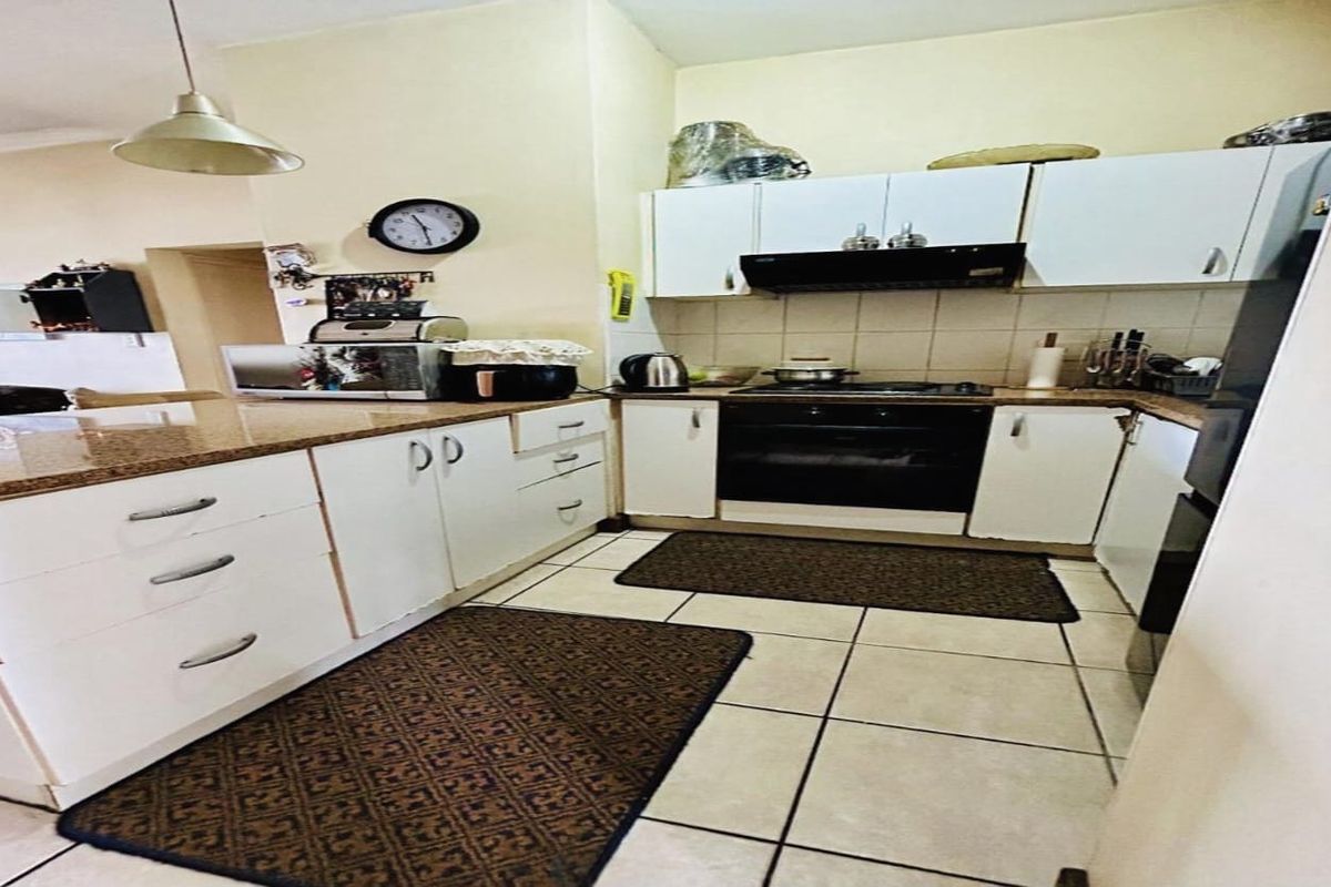 A functional kitchen featuring white cabinetry, granite countertops, built-in oven, hob, and tiled flooring, offering a practical layout for daily meal preparation.