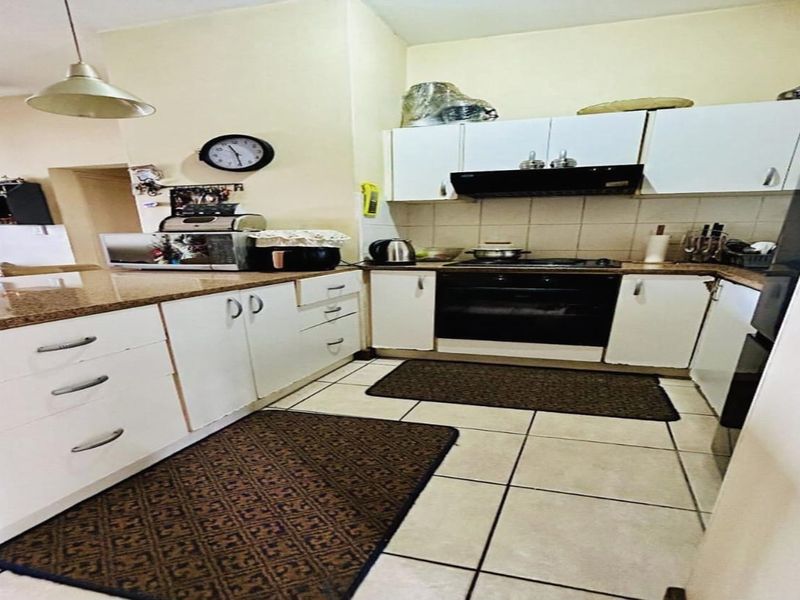 A functional kitchen featuring white cabinetry, granite countertops, built-in oven, hob, and tiled flooring, offering a practical layout for daily meal preparation.