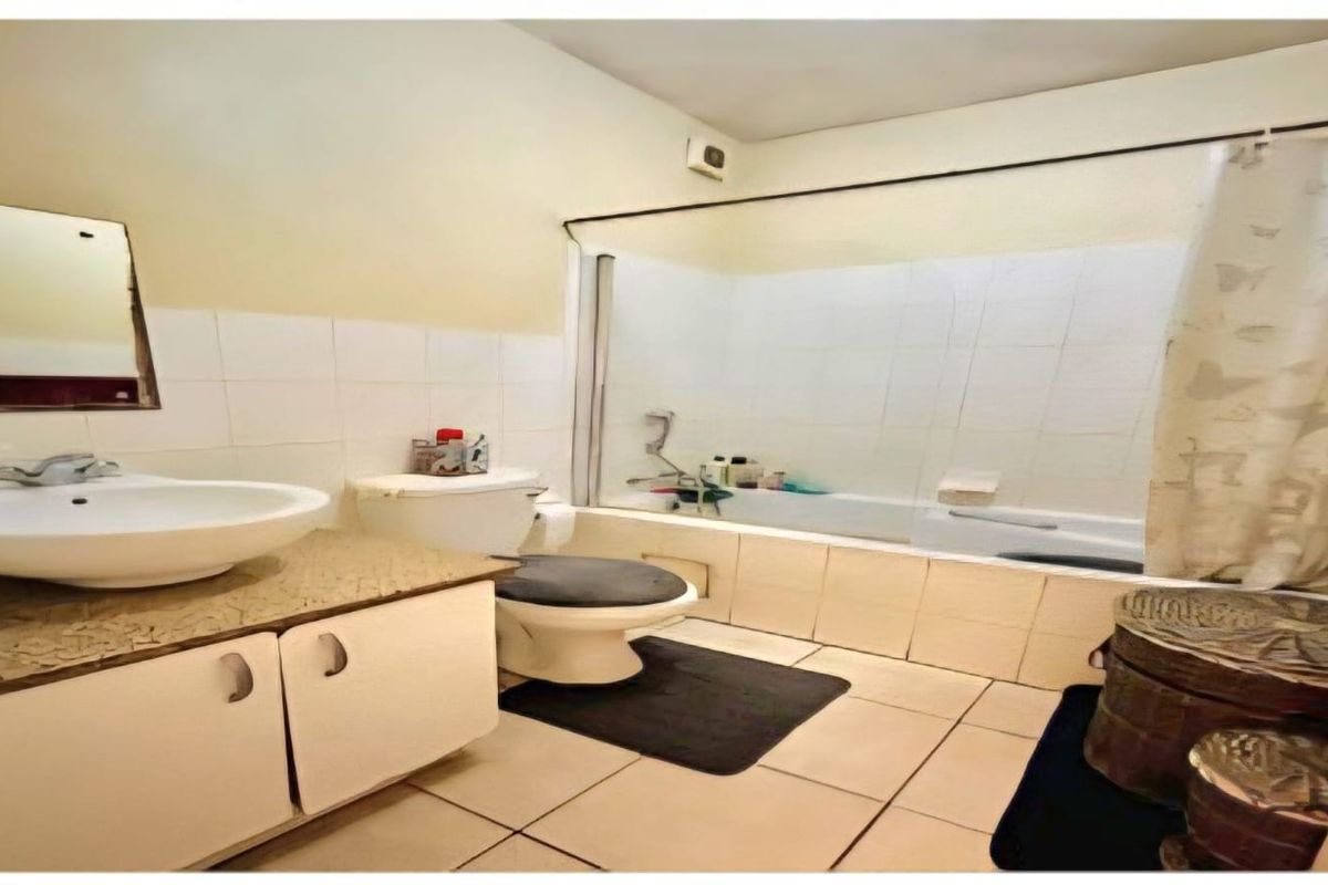 A dated bathroom featuring a vanity cabinet, ceramic basin, toilet, and a bathtub with shower mixer, finished with tiled walls and flooring.