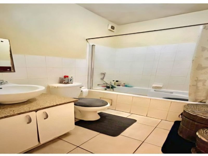 A dated bathroom featuring a vanity cabinet, ceramic basin, toilet, and a bathtub with shower mixer, finished with tiled walls and flooring.