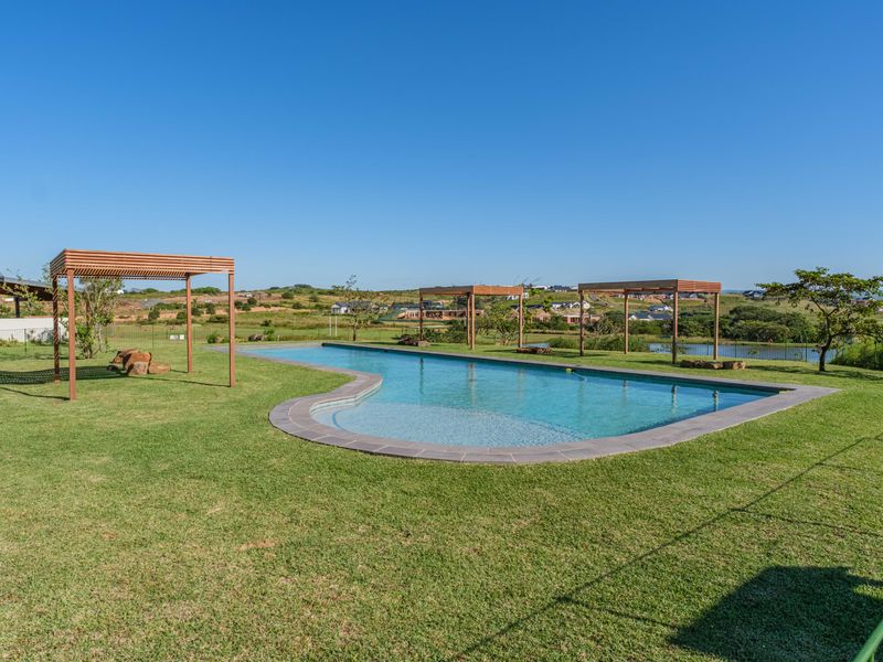 A well-maintained swimming pool area featuring multiple timber pergolas, expansive green lawn, and scenic views of the surrounding landscape.