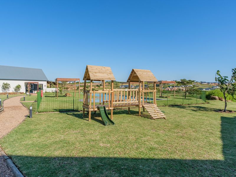 A well-maintained residential garden featuring a wooden playground structure, manicured lawn, gravel pathway, and secure perimeter fencing.