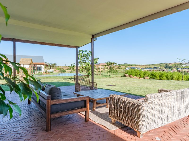 A spacious covered patio featuring brick paving, offering an expansive view of the landscaped garden and surrounding residential estate.