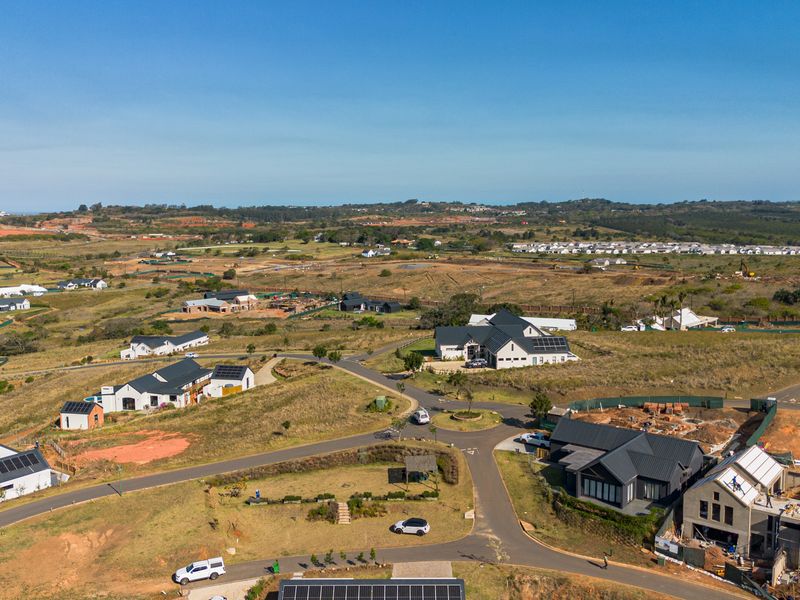 An aerial view of a developing residential estate featuring modern homes, paved road infrastructure, and surrounding natural landscape.