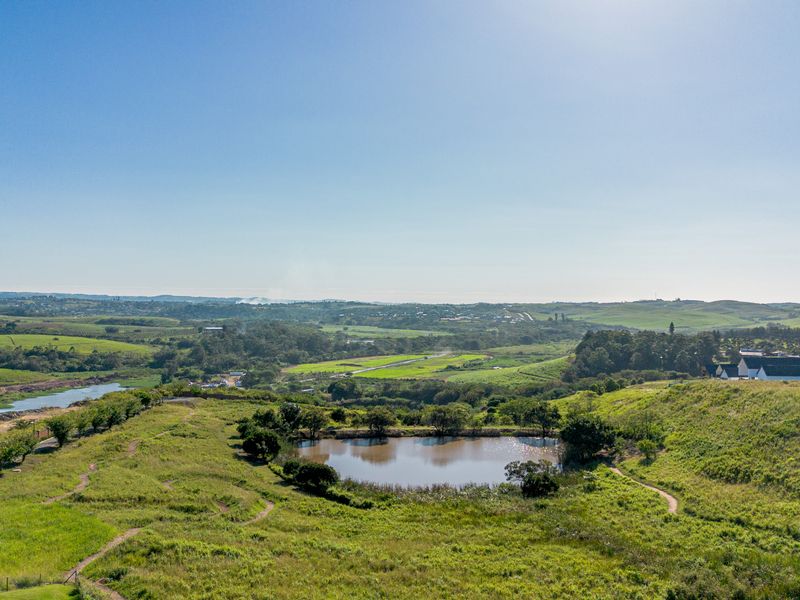 An aerial view of the vacant residential land featuring a natural pond, surrounding grassland, and established walking trails with scenic landscape views.