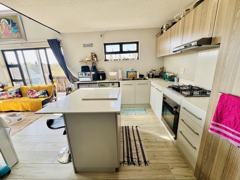 Open-plan kitchen and living area featuring a central island, modern cabinetry, gas hob, built-in oven, and sliding doors leading to an outdoor space.
