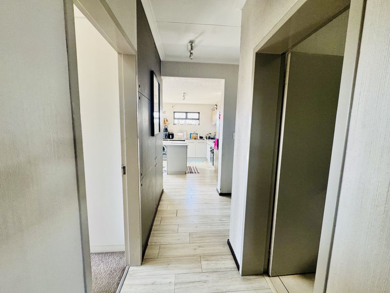 A bright hallway with light-toned tiled flooring, providing access to adjacent rooms and leading towards the kitchen area.