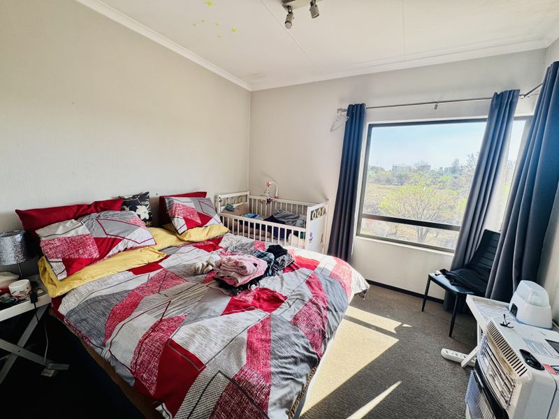 A functional bedroom featuring a large window that provides natural light and views, finished with carpeted flooring and standard ceiling lighting.