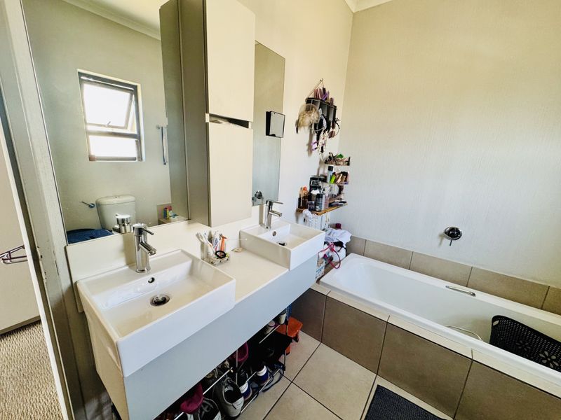 A functional bathroom featuring a double vanity with modern mixer taps, a built-in bathtub with tiled surround, and neutral floor tiling.