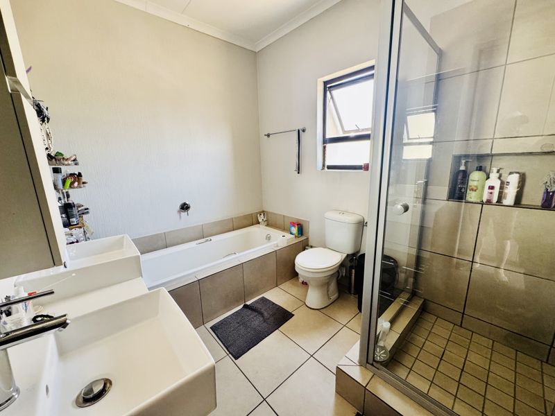 A functional bathroom featuring a glass-enclosed shower, a built-in bathtub, and a dual vanity setup with tiled finishes throughout.