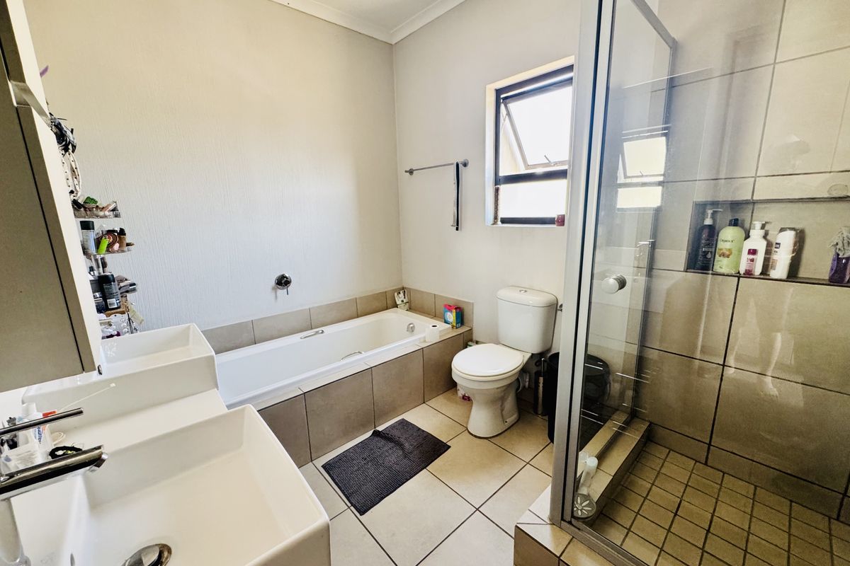 A functional bathroom featuring a glass-enclosed shower, a built-in bathtub, and a dual vanity setup with tiled finishes throughout.